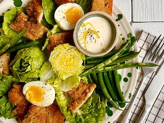 Caesarsalade met gepaneerde kalfslapjes, croutons, zachtgekookte eieren en groene groenten